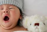 Asian baby yawning in bed next to stuffed animal bear - baby sleep guide