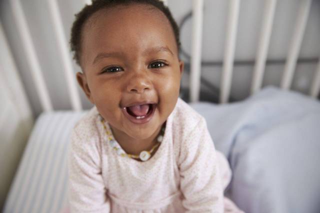 Black baby smiling in crib - baby sleep guide