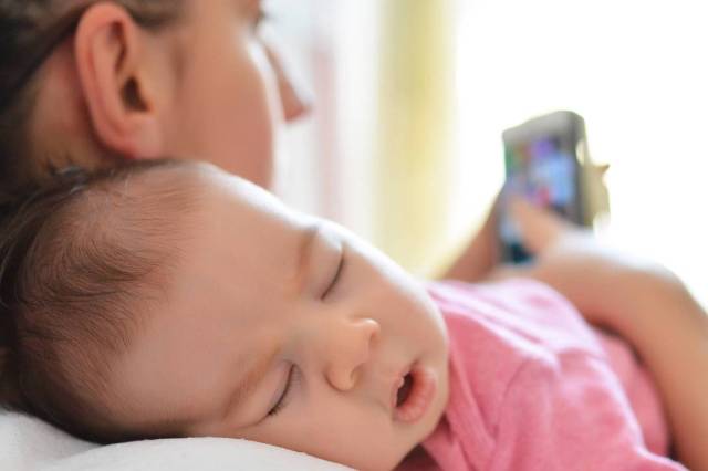 mother on phone with sleeping baby - baby sleep guide