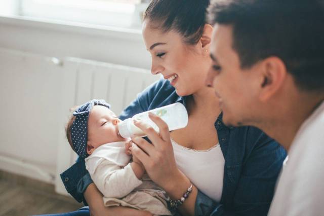 baby drinking from bottle with smiling parents - breastfeeding essentials