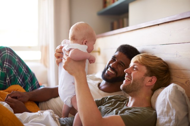 Loving Male Same Sex Couple Cuddling Baby Daughter In Bedroom At Home Together baby name inspiration