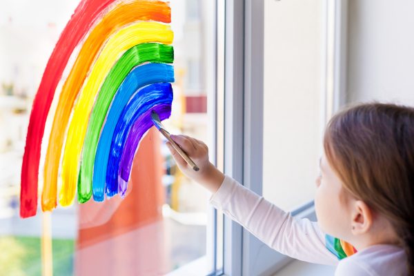 A child paints a rainbow on the window for Pride celebration