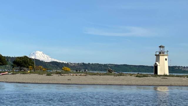 the lighthouse on a beach just outside the harbor with mt raininer in the background of gig harbor