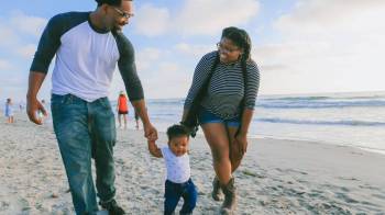 An African-American family enjoy the beach with a baby using baby beach hacks