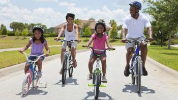 An African American family rides bikes together on a sunny day