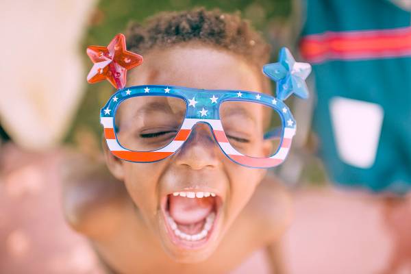 A boy smiles as he wears July 4th sunglasses