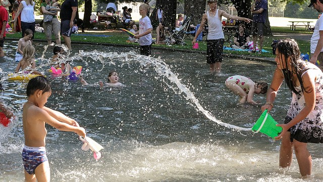 a mom splashes her son with a bucket of water at a seattle sprayparks wading pools