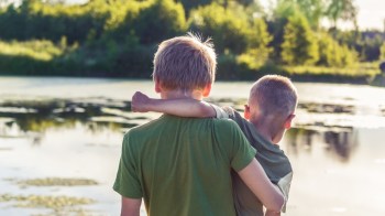 kid holding brother in front of a pond