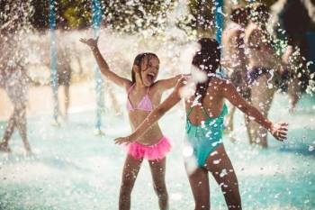 Two girls plays at a splash pad in summer