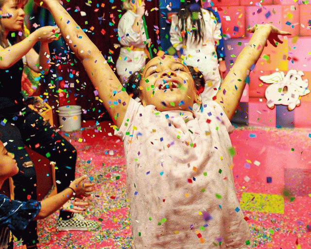A happy girl throws confetti into the air in the rainbow room of Candytopia
