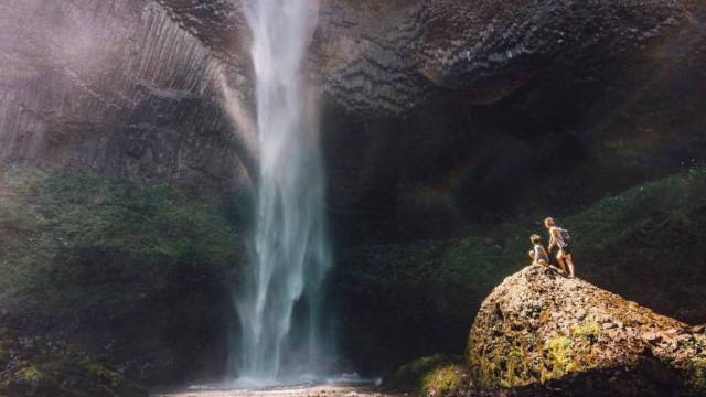 two people are perched on a rock at latourell falls near portland