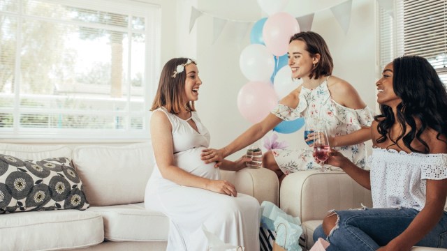 a woman touches a pregnant mom to bes belly while another woman looks on at a baby sprinkle shower