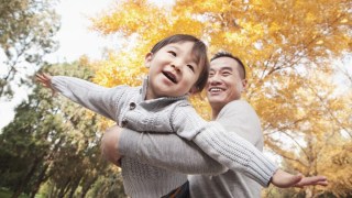 a young boy airplanes while his father spins him around in the fall sunshine