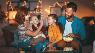 A mom, dad and their two kids laugh as they eat popcorn together during movie night, which is one of their favorite family traditions