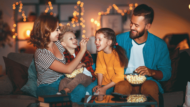 A mom, dad and their two kids laugh as they eat popcorn together during movie night, which is one of their favorite family traditions