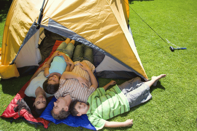 A mom, dad, son and daughter lay in front of a tent, starting the family tradition of camping out in their backyard
