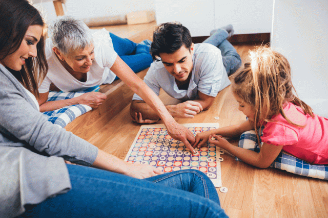 a mom, dad, daughter and grandparent lay on a wooden floor playing a game together