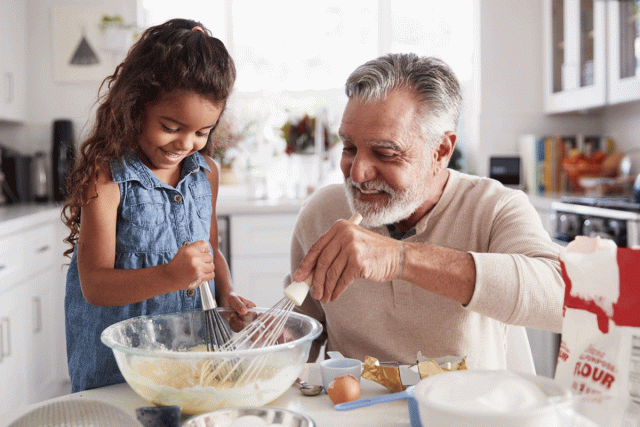 A girl and her grandfather are in the kitchen cooking together