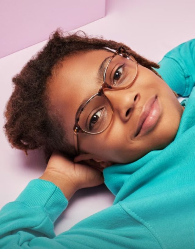 child wearing teal hoodie laying on their back wearing eyeglasses