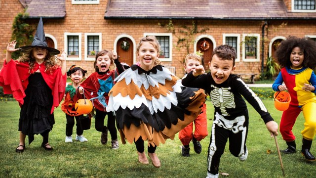kids in costumes run in a group after trick or treating with a house behind them