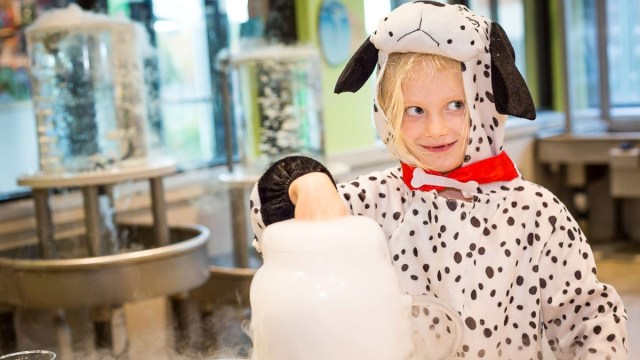 a girl dressed in a dalmation costume sticks her hand in a pretend potion at KidsQuest Children's Museum in Bellevue during a Halloween event in Seattle