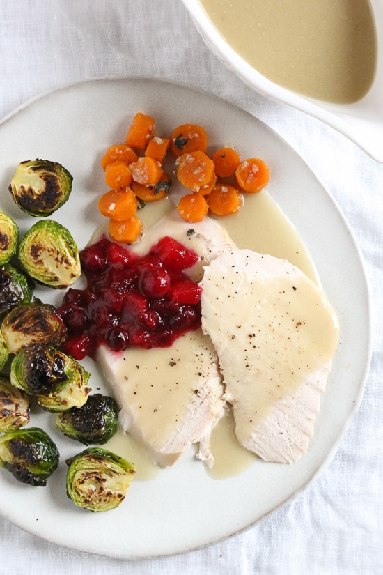 Slow cooker turkey breast sits on a plate next veggie sides and a gravy boat