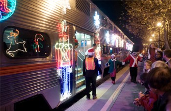 People walking by a train from Caltrain decorated with Christmas lights and festive displays like Nutcrackers and reindeer on the outside of the train.