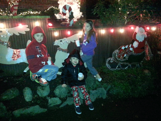 Three kids sit on a display of Santa and his sleigh at Candy Cane Lane in Seattle