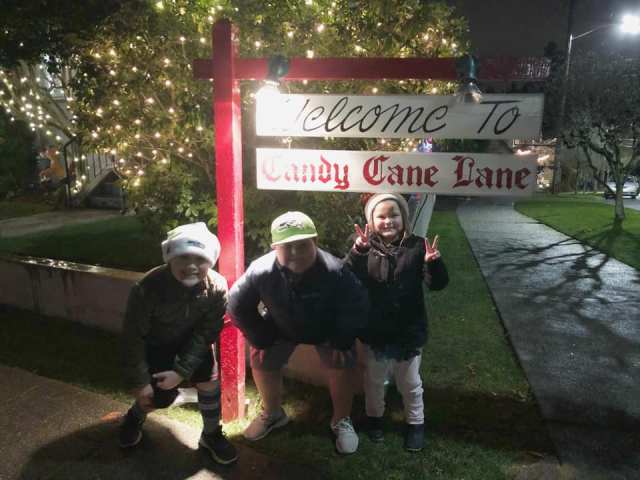Three kids pose under the Candy Cane Lane sign next to lights in Seattle