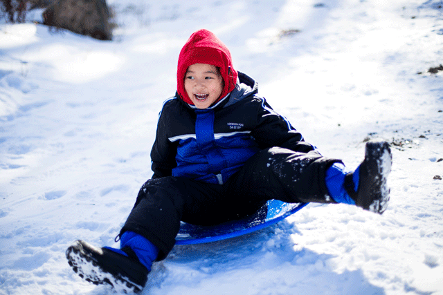 A happy boy slides down a snowy hill near Portland on a blue sled