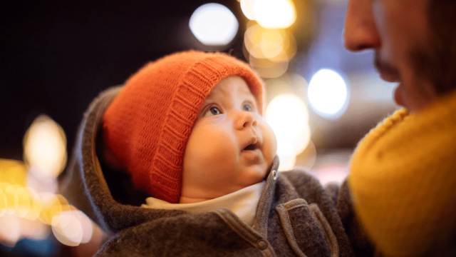 A baby born in December looks at his father under Christmas lights