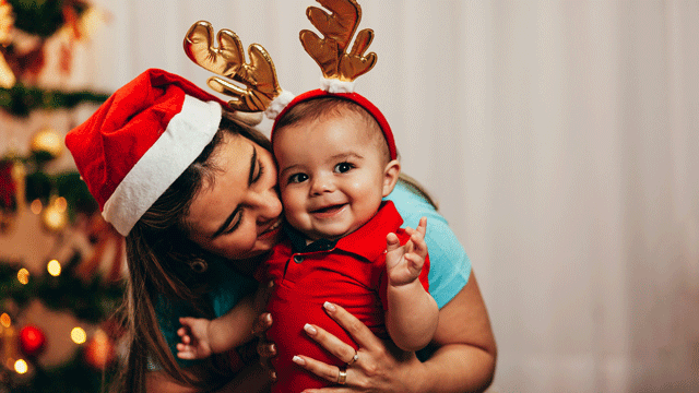 A mom kisses her December baby on the cheek in front of a Christmas tree
