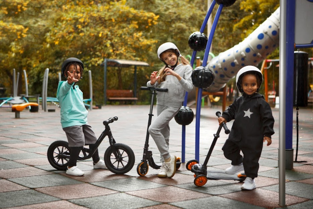 three kids riding scooters and balance bikes