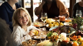 a girl smiles during Thanksgiving dinner in Seattle with food and family in the background