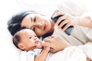 a mom and baby on the bed looking at mom's phone where she's using the best baby tracking apps