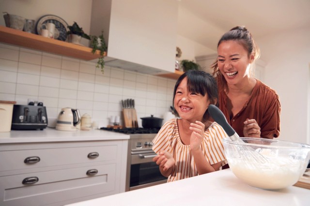 A mom and daughter laugh in the kitchen as they make butter together