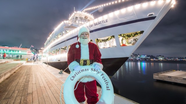 Santa stands in front of a Seattle Christmas Ship festival boat with a bouy