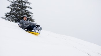 A boy goes sledding in boston uses a yellow slide on a snowy slope