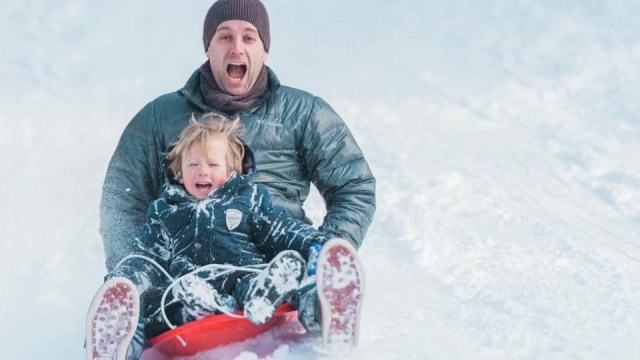 a kid and father come racing down a snowy hill in a sled while snow tubing mt hood near portland