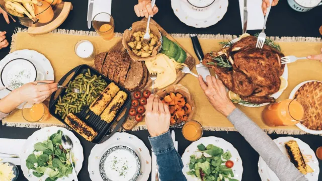 Hands are shown digging in to a big take-home Thanksgiving dinner with turkey, corn, pie and more