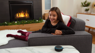 A girl sits in her living room next to a fire place using Alexa Christmas skills