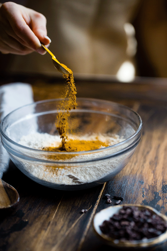 A clear mixing bowl on a table with bright yellow ingredients being stirred into another ingredient
