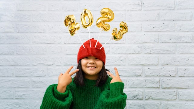 a kid wearing a 2023 new years eve hat and holding up peace signs