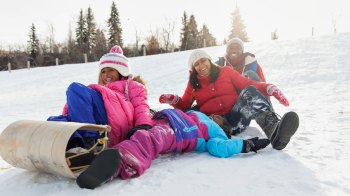 Black family laughing while sledding down snowy hill