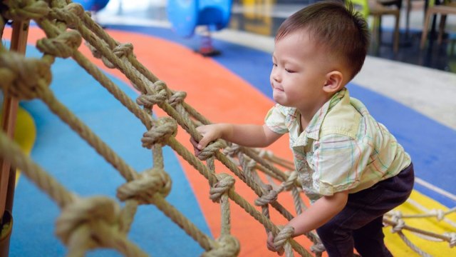 A boy climbs a rope ladder at an indoor playground Boston