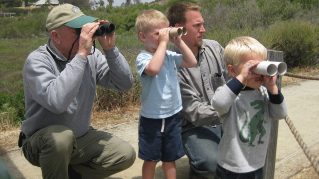 Two boys look through handmade binoculars with help from two adults at San Elijo Lagoon Ecological Reserve and Nature Center during a ranger program for kids