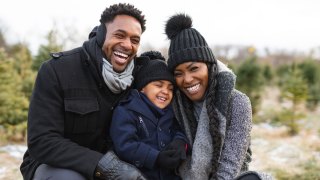 A black family in winter wear sits outside snuggling before going for a hike