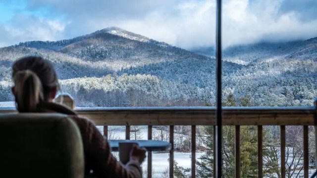 a woman sit on a porch looking at snow covered mountains outside of Atlanta ga cabin rentals with a cup of coffee in hand