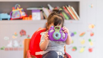 a child sits on a red chair with a toy camera at a drop in childcare near portland spot