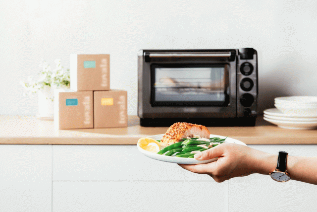 Someone holds a plate of salmon and veggies from the meal delivery service Tovala and prepares to place it in the service’s signature Smart Oven.